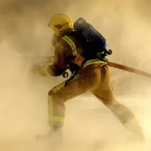 Firefighter with hose blasting flames, surrounded by smoke and steam.
